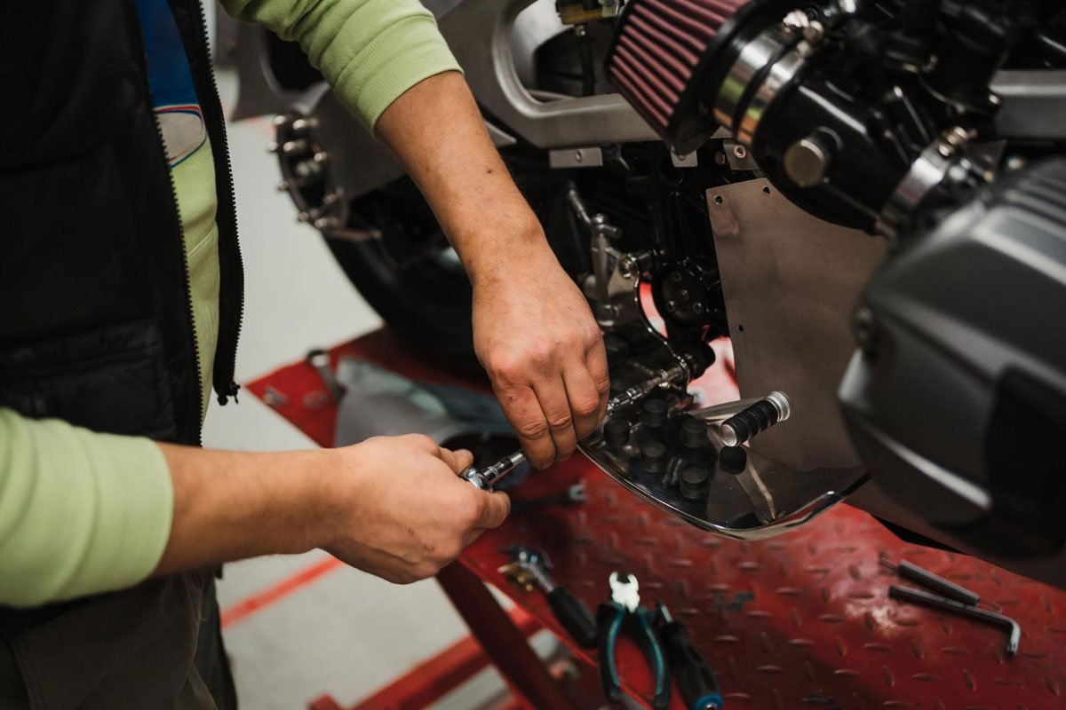 a mechanic uses a socket wrench on an exposed motorcycle assembly beside tools on a workshop life
