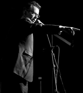john hegley comedian pointing on stage black white