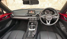 Interior view of red Mazda Mx 5 Sport with black leather steering wheel and gear showing two seats and dashboard sat nav and mirror