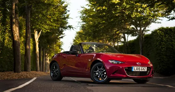 Mazda M X 5 sport side view red car on a tree lined road in the sun top down convertible nice